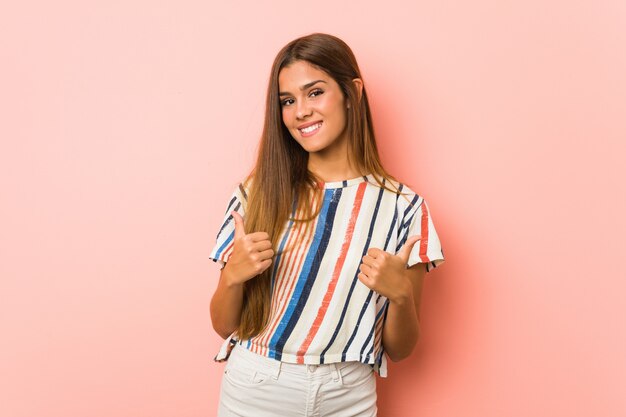 Young slim woman raising both thumbs up, smiling and confident.