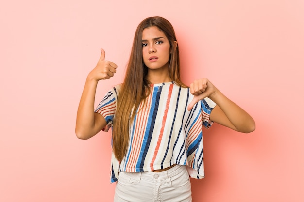 Young slim woman showing thumbs up and thumbs down, difficult choose concept