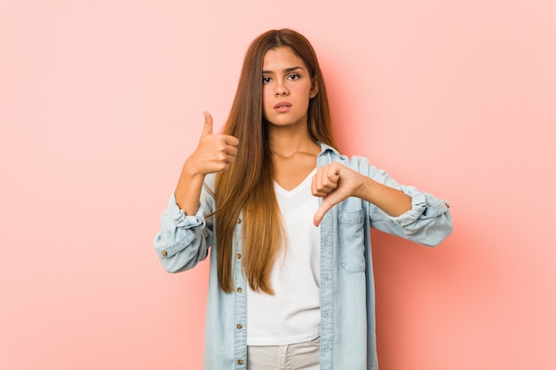 Young slim woman showing thumbs up and thumbs down, difficult choose concept