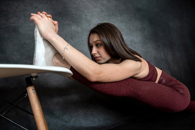 Young slim woman in sport cloth doing split stretching exercise against dark background