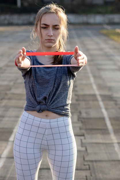 Foto giovane donna sottile in abbigliamento sportivo che fa squat con una fascia di gomma su una pista di stadio rivestita di nero