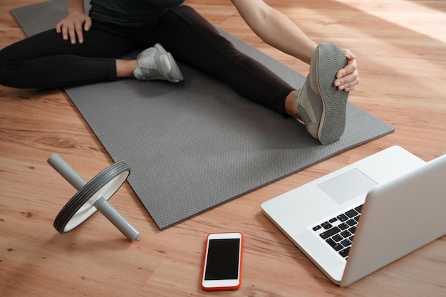Молодая стройная женщина растягивает ноги во время онлайн-тренировки дома