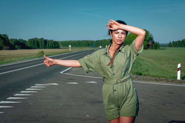 Photo young slim woman in a tight overalls is trying to catch a car in the middle of the road