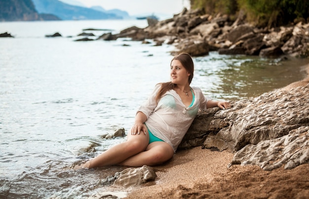 Giovane donna magra in camicia bagnata bianca sdraiata sulla riva del mare