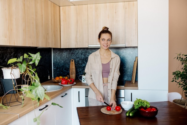 Young slim woman with bun hairstyle cooks vegetables in the kitchen in scandinavian interior style