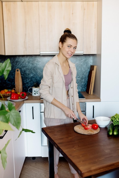 Young slim woman with bun hairstyle cooks vegetables in the kitchen in scandinavian interior style