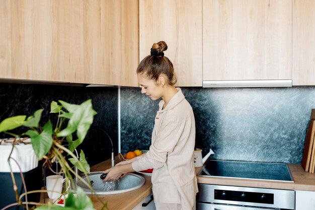 お団子の髪型の若いスリムな女性は、スカンジナビアのインテリアスタイルでキッチンで野菜を調理します