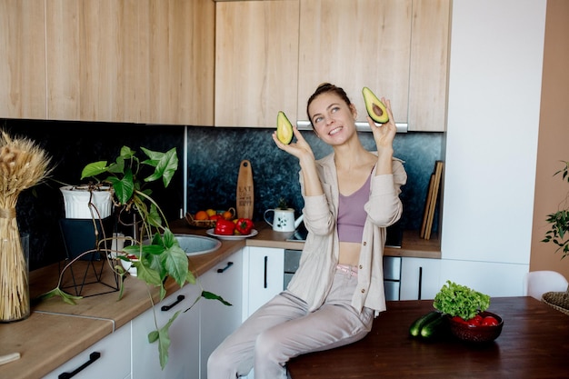 La giovane donna snella con l'acconciatura da panino cuoce le verdure in cucina in stile interno scandinavo