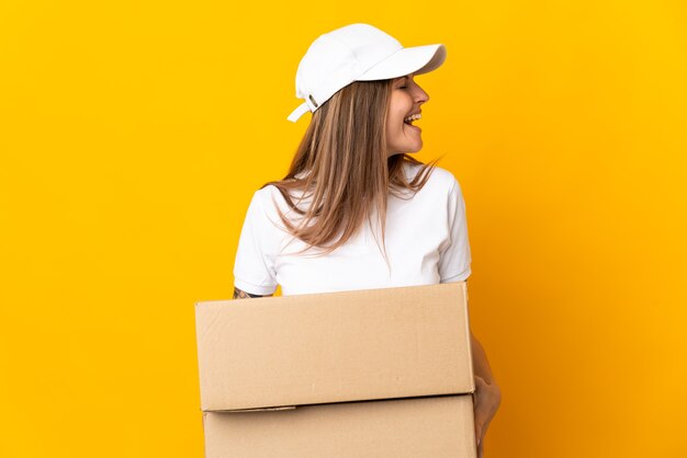 Young slovak delivery woman isolated on yellow background laughing in lateral position