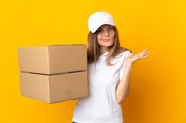 Young slovak delivery woman isolated on yellow wall having doubts while raising hands