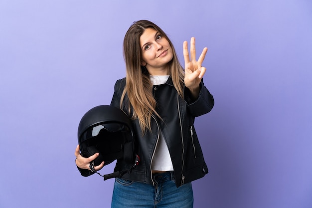 Young slovak woman holding a motorcycle helmet isolated on purple  happy and counting three with fingers