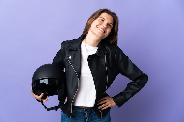 Young slovak woman holding a motorcycle helmet isolated on purple  posing with arms at hip and smiling