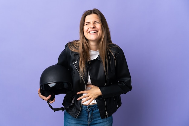 Young slovak woman holding a motorcycle helmet isolated on purple  smiling a lot