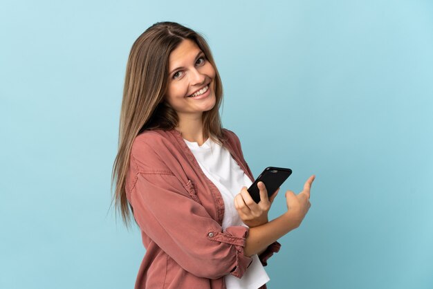 Young Slovak woman isolated using mobile phone and pointing back