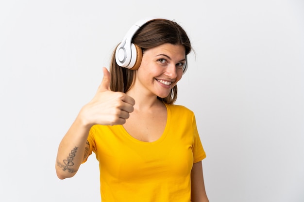 Young slovak woman isolated on white wall listening music and with thumb up