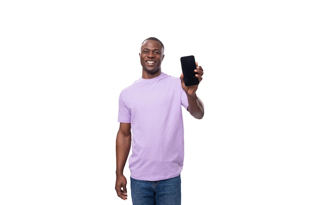 Young smart african man dressed in a lilac tshirt and jeans shows a smartphone mockup