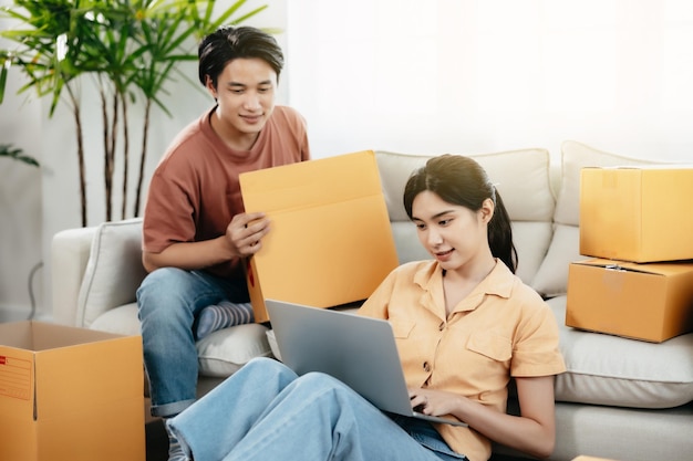 Young smart Asian couple SME owners entrepreneurs surround by boxes online working from home