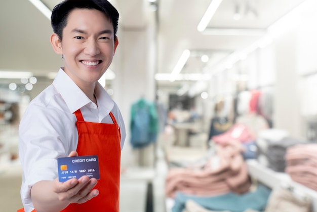 Photo young smart attractive asian male reatuarant owner hand sign ok with credit card online purchase order online from home concept asian apron uniform smile warm welcome for appllication order