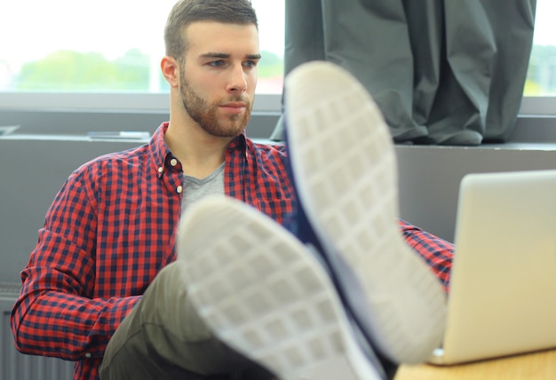 똑똑한 젊은이들은 현대 사무실에서 열심히 일하면서 가제트를 사용하고 있습니다. 그의 노트북에서 작업 하는 젊은 남자.