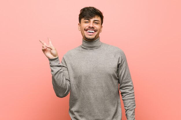 Young smart student man joyful and carefree showing a peace symbol with fingers.