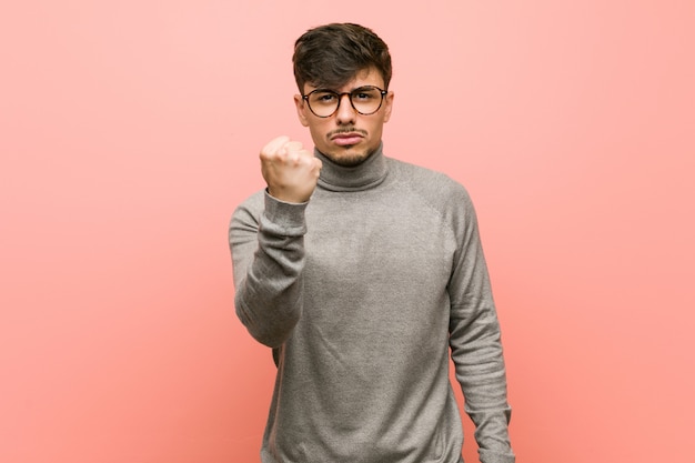 Young smart student man showing fist to camera, aggressive facial expression.