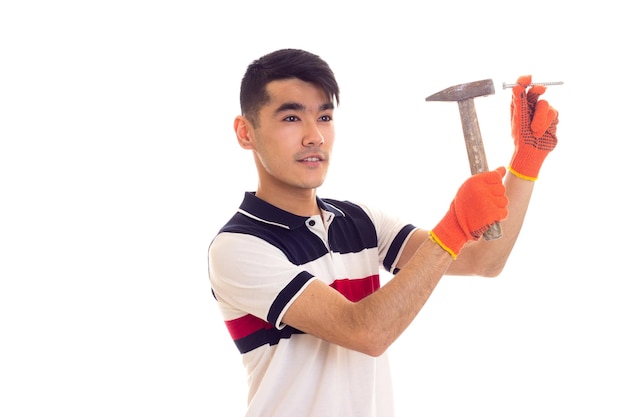 Young smartlooking man with dark hair in white and blue t-shirt and orange gloves holding a hummer and nails on white background in studio