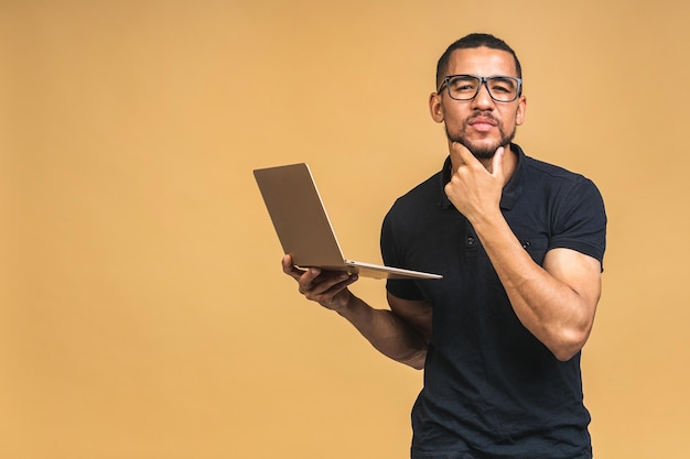 Giovane sorridente afroamericano nero uomo in piedi e utilizzando il computer portatile isolato su sfondo beige