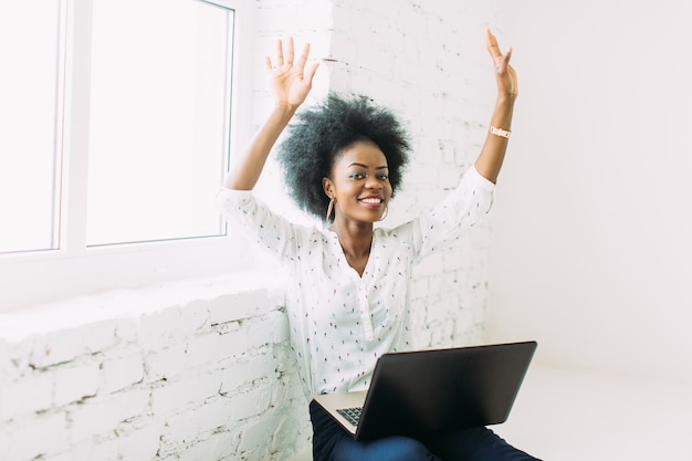 Young smiling african american business woman using the laptop, sitting on the floor