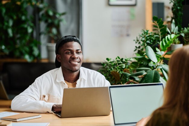 Young smiling african american businessman with laptop looking at colleague