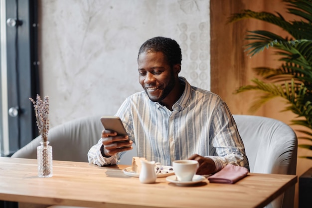 スマートフォンの画面を見ている若い笑顔のアフリカ系アメリカ人の男性マネージャー