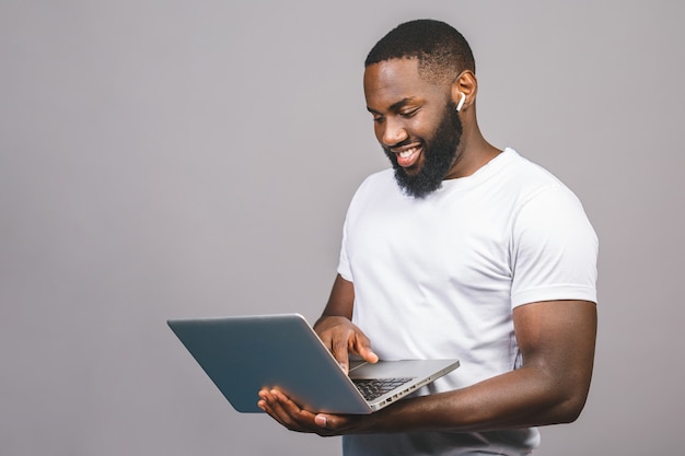 영 아프리카 계 미국인 남자 서 회색 배경 위에 고립 된 랩톱 컴퓨터를 사용 하여 웃 고.