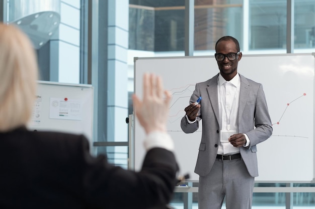 Young smiling african american teacher pointing at female broker raising hand