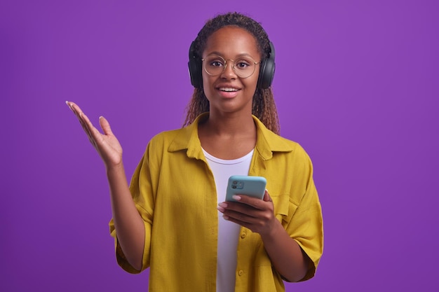 Young smiling african american woman listens to music on headphones with phone