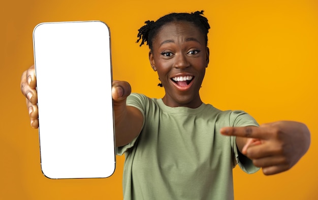 Young smiling african american woman showing smartphone with blank screen against yellow background