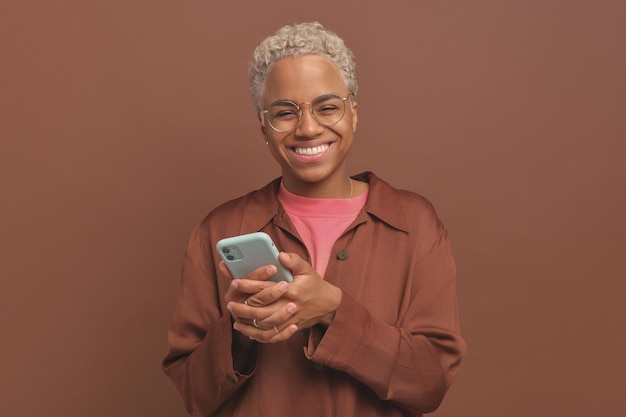Young smiling african american woman with phone stands in brown studio