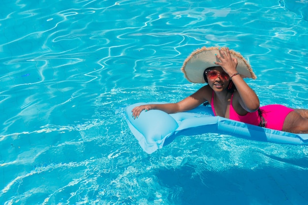 비키니 입은 젊은 미소 아프리카 소녀, 수영장에서 부풀릴 수 있는 밀짚 모자를 쓰고 있습니다.