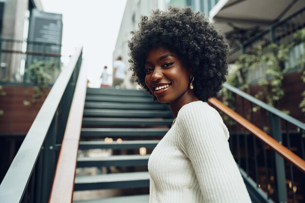 街の階段の近くでポーズをとる若い笑顔のアフリカ人女性