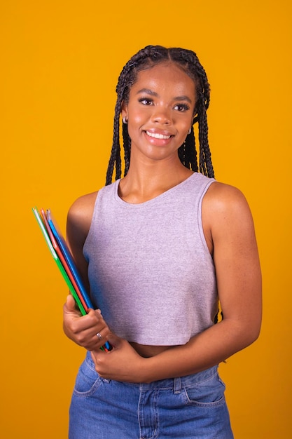 Young smiling afro girl happy teenage student holding books and notebooks on background with free space for text