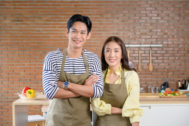 Young smiling asian couple wearing an apron in the kitchen room cooking concept