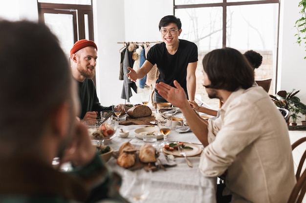 写真 嬉しそうにテーブルに寄りかかって眼鏡と黒のtシャツの若い笑顔のアジア人男性