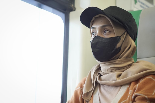 Young smiling asian woman in hijab sitting in a train and looking out the window going on vacation