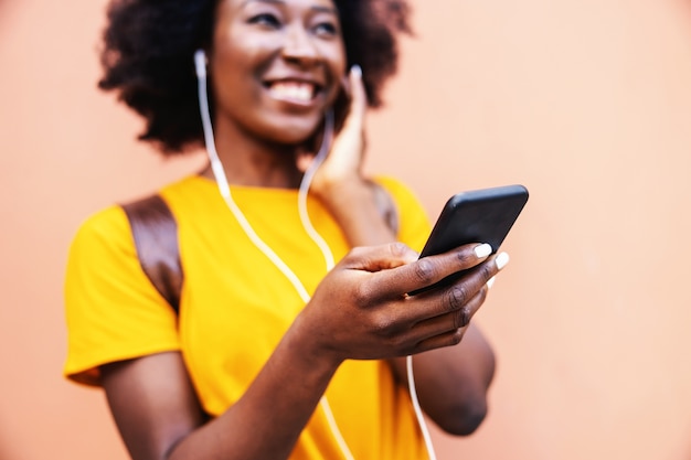 Молодая улыбающаяся привлекательная африканская женщина улыбается, слушает музыку и держит смартфон. селективный фокус под рукой.