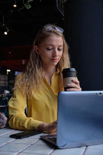 Young smiling attractive cauasian woman sitting at table typing on laptop keyboard at coffee shop