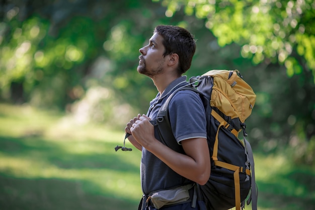 Photo young smiling backpack man in summer forest nature. happy handsome male adult student looking at camera walking hiking in forest background. school bag or backpacking travel concept.