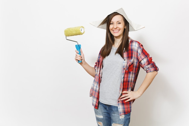 Young smiling beautiful woman in casual clothes and newspaper hat holding roller for wall painting isolated on white background. Instruments, tools for renovation apartment room. Repair home concept.