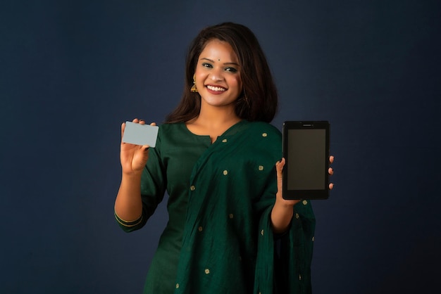 Молодая улыбающаяся красивая женщина или девушка, представляющая кредитную карту при использовании мобильного телефона или смартфона.