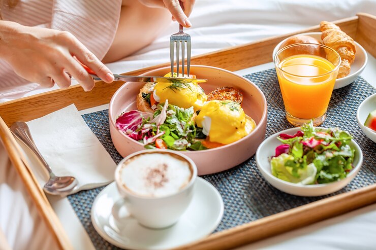 Photo 居心地の良いホテルの部屋のベッドで朝食をとっている若い笑顔の美しい女性