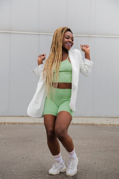 Young smiling black woman with long blond braids dancing in the street. Vertical image.