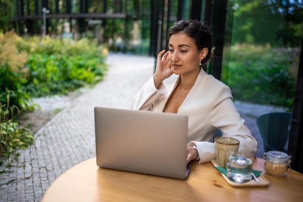 Young smiling brunette business woman in stylish smart dress working on laptop in cafe at street of Prague