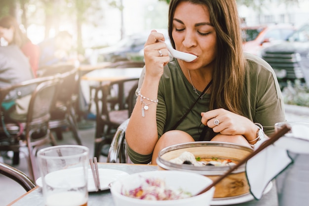 Foto ragazza castana sorridente dei giovani che mangia dim sum nel caffè asiatico della via